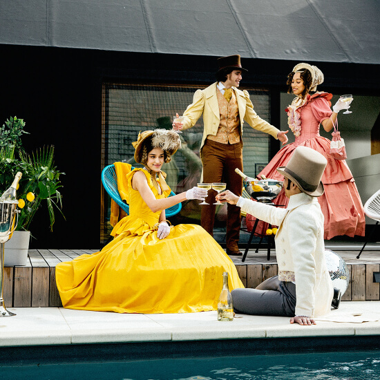 Gruppe von Leuten in alter Kleidung beim Feiern am Pool mit einer Flasche Schlumberger 180 Jahre Limited Edition