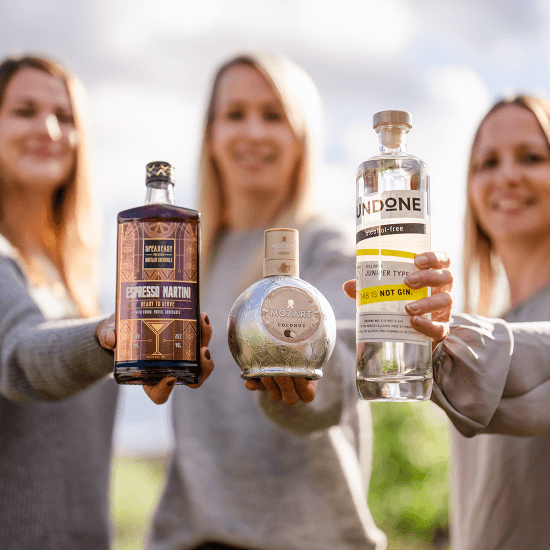 Drei Frauen halten jeweils eine Flasche Speakeasy Espresso Martini, Mozart Chocolate White und Undone Gin in die Kamera.
