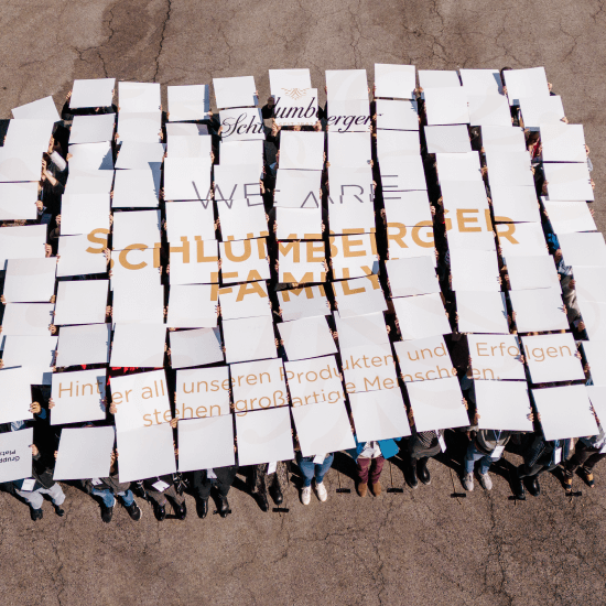 Eine Gruppe aus Schlumberger Mitarbeitern auf einem Parkplatz von oben fotografiert. Jeder hält ein Schild in Händen, das ein gemeinsames Bild ergibt.