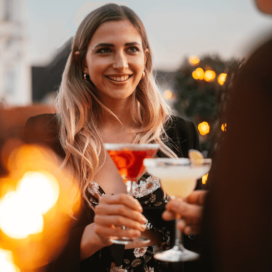 Frau lächelt ihren Gesprächspartner an und hält ihm einen Cocktail hin