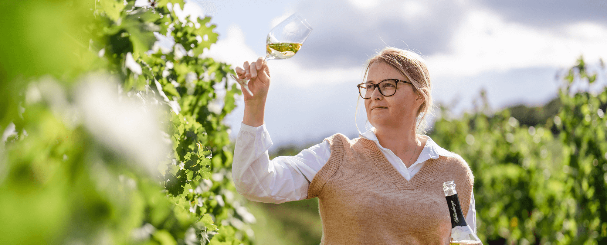 Frau begutachtet Weinglas zwischen Weinreben