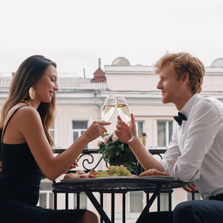 Ein Paar sitzt schön gekleidet auf der Terrasse, isst und trinkt Sekt.