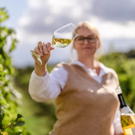 Frau begutachtet Weinglas zwischen Weinreben