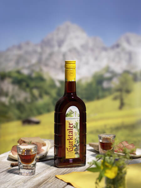 In neuer Tracht: Gurktaler der Milde Alpenkräuter 0,7l mit Berglandschaft im Hintergrund
