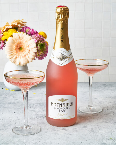 Hochriegl Alkoholfrei Rosé 0,75l mit zwei Gläsern auf Tisch und Blumen im Hintergrund